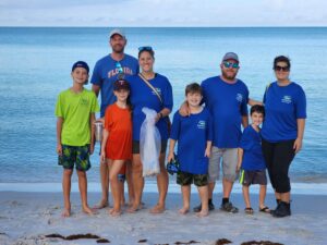 A family smiling and posing together for a photo on a sandy beach with the ocean in the background.